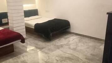 A room with a marble floor, a bed with a red headboard, a black ottoman, and a white pillar.