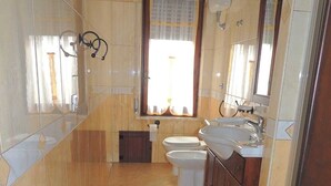 A bathroom with a toilet, bidet, and sink, tiled floor, and a window with curtains. - Vacation apartment in Santa Maria Navarrese, beautiful view (Santa Maria Navarrese)