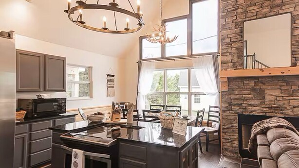 Une cuisine moderne dotée d’un îlot central, un coin repas avec une table et des chaises, une cheminée et un espace salon confortable avec un canapé.