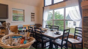 Un espace repas comprenant une grande table, des chaises, un lustre et une vue sur l’extérieur.