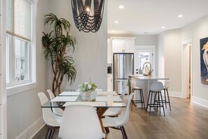 Une cuisine moderne dotée d’appareils électroménagers en acier inoxydable, d’une table à manger en verre et de chaises blanches.