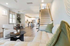 A spacious living room with a sofa, a dining area, and a kitchen in the background. - New Home | Community Pool | 0.2 mi to Beach Access (Carolina Beach)