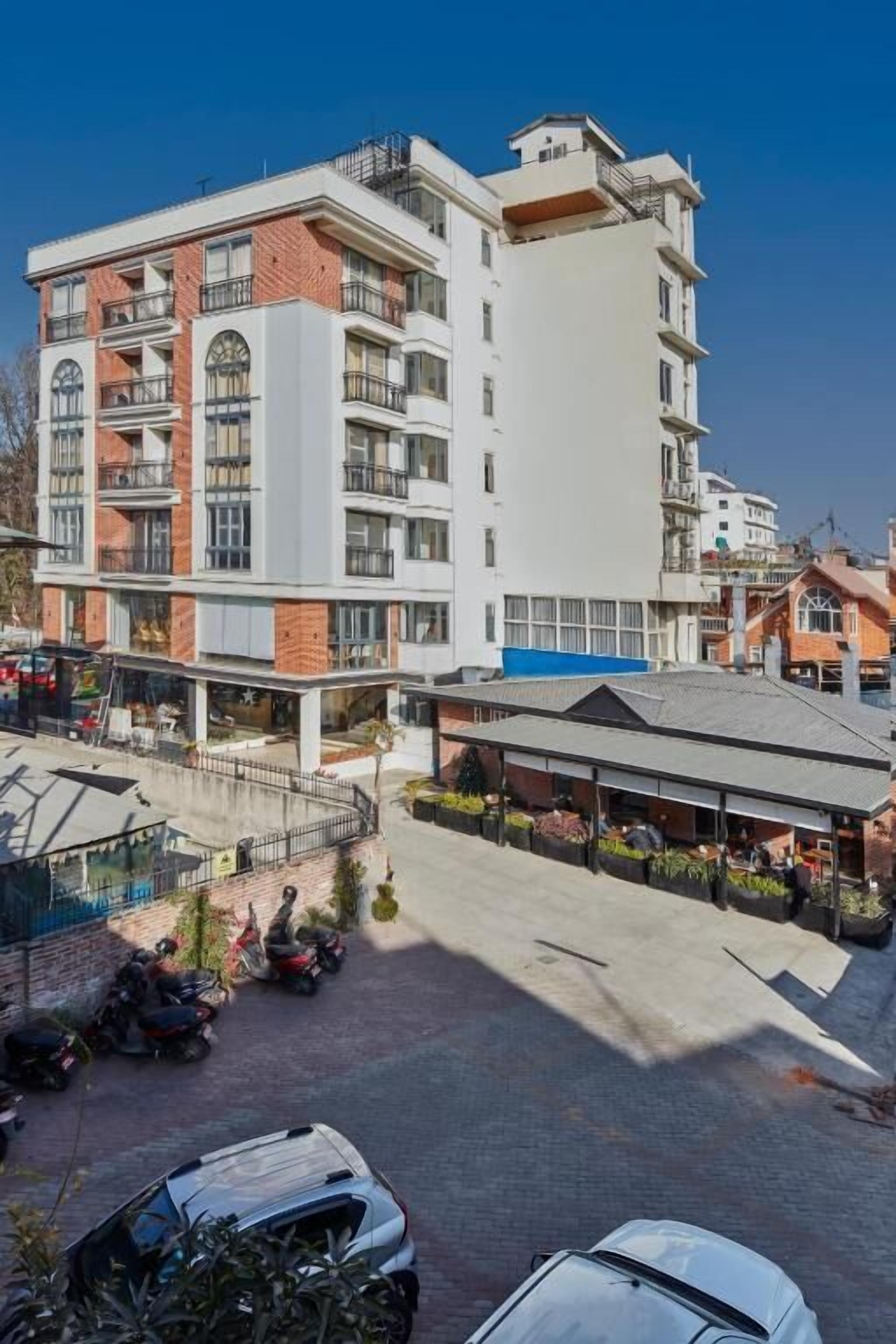A multi-story building with balconies, a covered outdoor area, and parked vehicles.