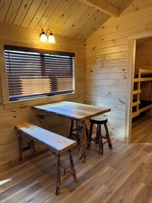 Un interior de madera con una mesa, bancos, una ventana con persianas y una escalera de madera.