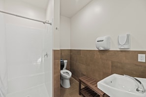 Une salle de bain équipée d’une douche, de toilettes, d’un lavabo et d’un petit banc en bois.