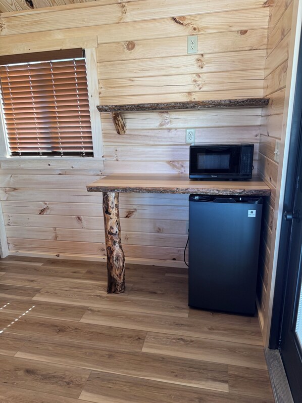 Eine kleine Küche mit Holzwänden, einer eingebauten Mikrowelle, einem kleinen Kühlschrank und einem Fenster mit Jalousien.