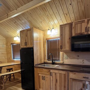 A wooden interior with a kitchen area featuring cabinets, a refrigerator, a sink, and a bench.
