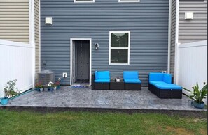 A patio with a gray house, a white fence, and a blue outdoor seating area.