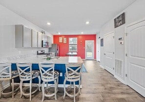 A modern kitchen with a central island, bar stools, and a red accent wall.