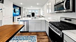 Una cucina moderna con mobili bianchi, forno a microonde integrato, piano cottura e lavastoviglie.