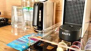 Un comptoir de cuisine avec une machine à café, une bouilloire, une bouteille d’eau, un verre et un paquet de crème pour café.