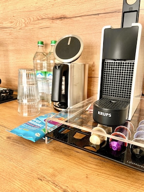 A kitchen counter with a coffee machine, a kettle, a water bottle, a glass, and a packet of coffee creamer. - Forest & Wind - Nature Meets Modernity (Marburg)