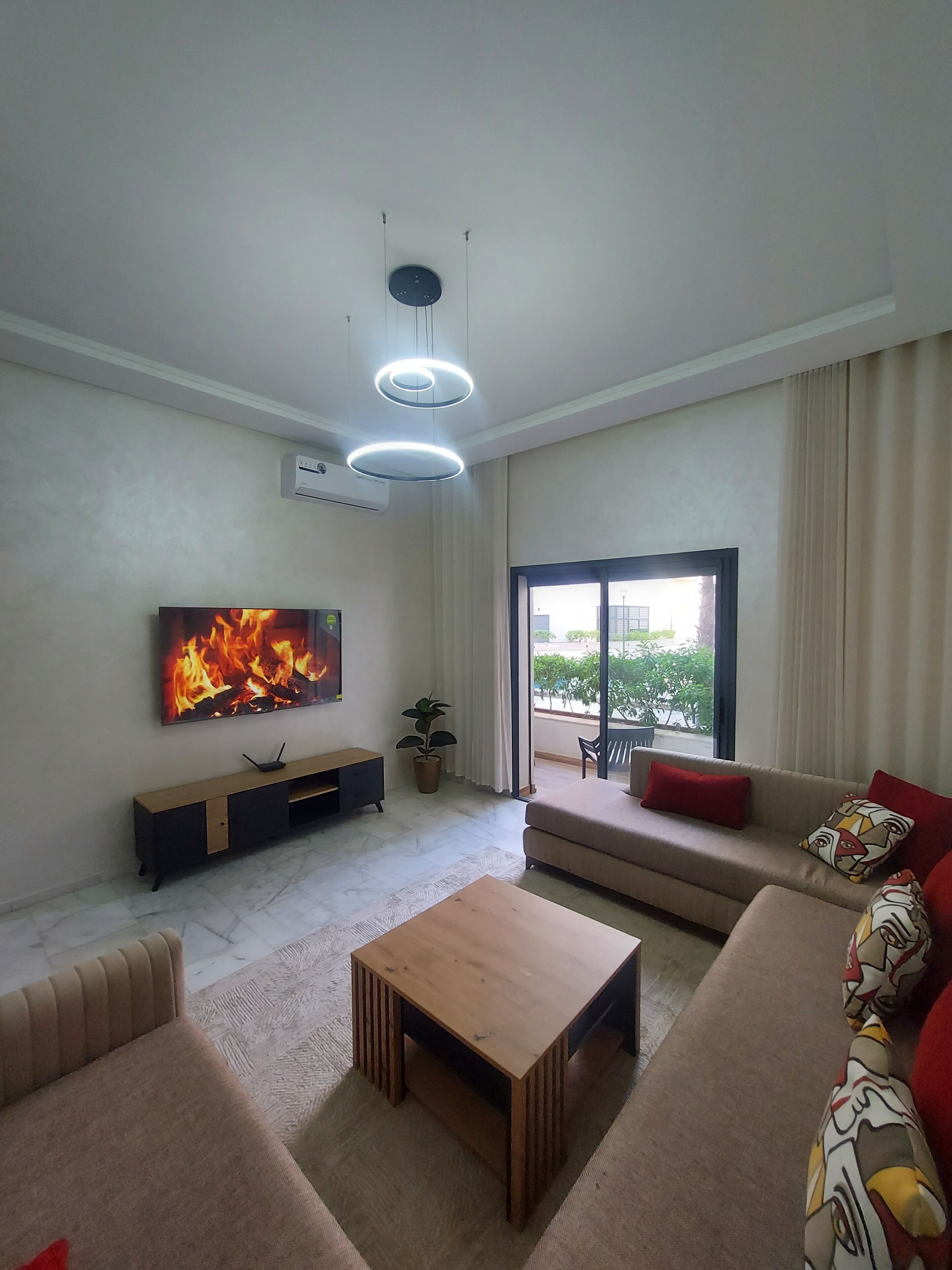 A modern living room with a flat-screen TV, a wooden coffee table, a sofa, and a sliding glass door leading to a balcony.