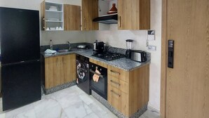 A modern kitchen with a black refrigerator, wooden cabinets, a built-in oven, and a granite countertop. - Quiet, Modern Studio Apartment in Zenata with Pool View (Âïn-Harrouda)