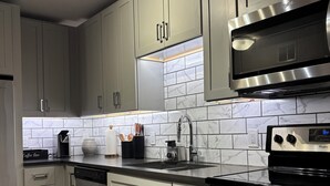 A kitchen with grey cabinets, a stainless steel microwave, and a digital clock. - Welcome to your home away from home. A calm, escape designed for pure relaxation (Decatur)