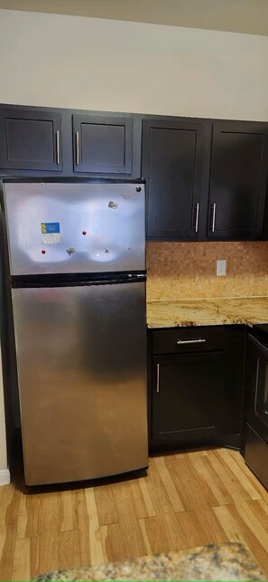 Eine Küche mit einem Edelstahl-Kühlschrank, schwarzen Schränken, einer Holzarbeitsplatte und einem Geschirrspüler.