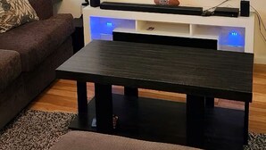 Ett vardagsrum med en platt-TV som är monterad på väggen, ett mörkt träbord och en brun soffa.