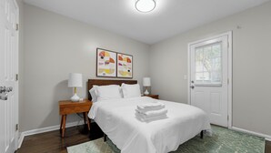 Una camera d'albergo con un letto, due comodini, un tavolo da notte, una porta con finestra e una lampada a soffitto.