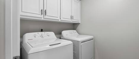 A laundry room with two white washing machines, a white cabinet above, and a light-colored wall.