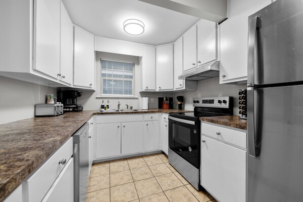 Una cocina moderna con armarios blancos, un refrigerador de acero inoxidable, horno empotrado y encimera de granito.