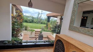 Una stanza con pavimento in legno, uno specchio grande e vista su un giardino con piante e un vialetto.