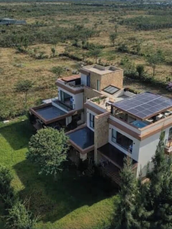 A modern, multi-story house with a flat roof, large windows, and solar panels.