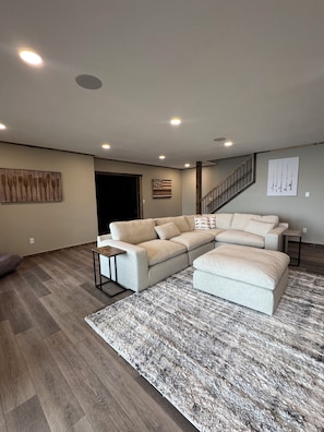 A living room with a sectional sofa, a small table, a rug, and a staircase.