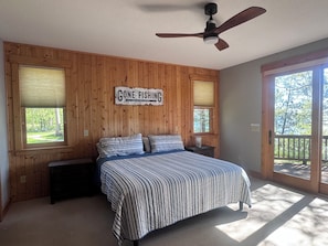A bedroom with a bed, a ceiling fan, a window with blinds, and a sign on the wall.