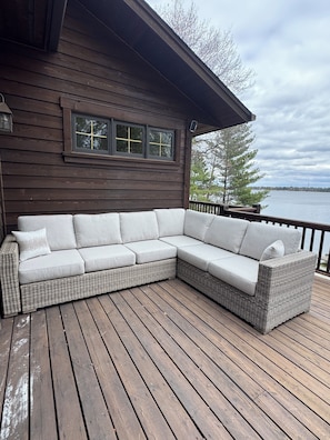 A wooden deck with a wicker sectional sofa and a window with a cross design.