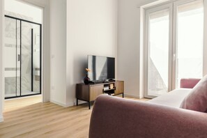 Ein modernes Schlafzimmer mit einem großen Bett, einem Fernseher auf einer Holzkommode und einer Glasraumtür, die auf einen Balkon führt.