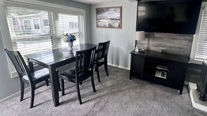Un coin repas avec une table et des chaises en verre, un meuble de rangement noir pour les appareils multimédias et un ventilateur de plafond.