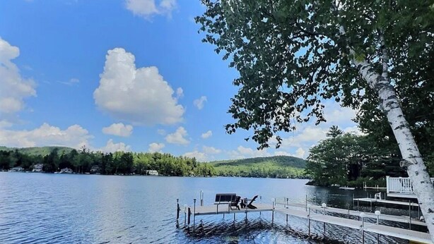 Un lac paisible, avec une jetée qui s’avance sur l’eau, entouré d’arbres et de collines.