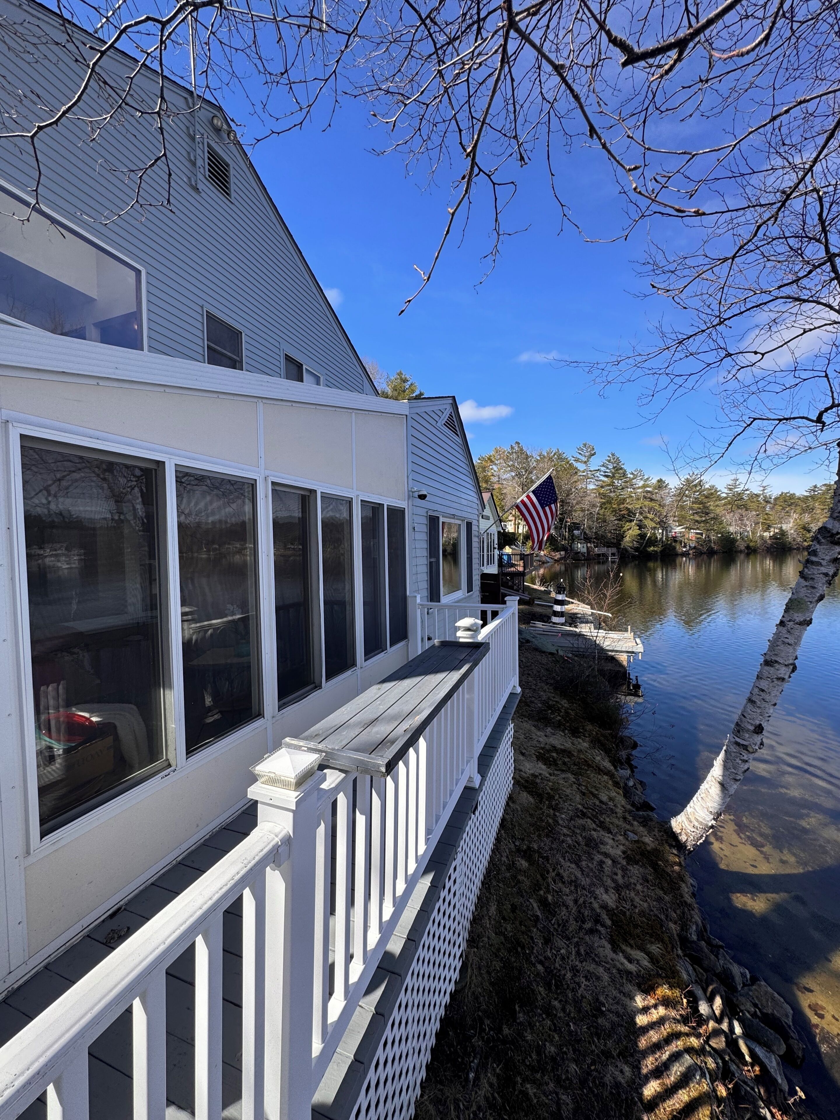 A waterfront house with a deck, large windows, and an American flag.