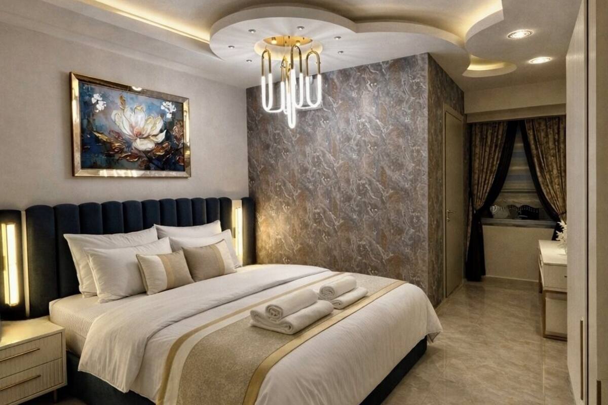 Une chambre moderne avec un grand lit, une tête de lit dotée d’un éclairage intégré, un mur à motifs de marbre et un luminaire au plafond.