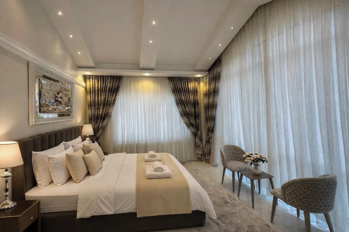 Une chambre spacieuse avec un grand lit, une table de chevet, une chaise et une table ornée d’un vase de fleurs.