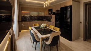 A modern kitchen with a dining area, featuring a central island, pendant lighting, and a large flat-screen TV. - Villa Nuri Konaklama (Antakya)