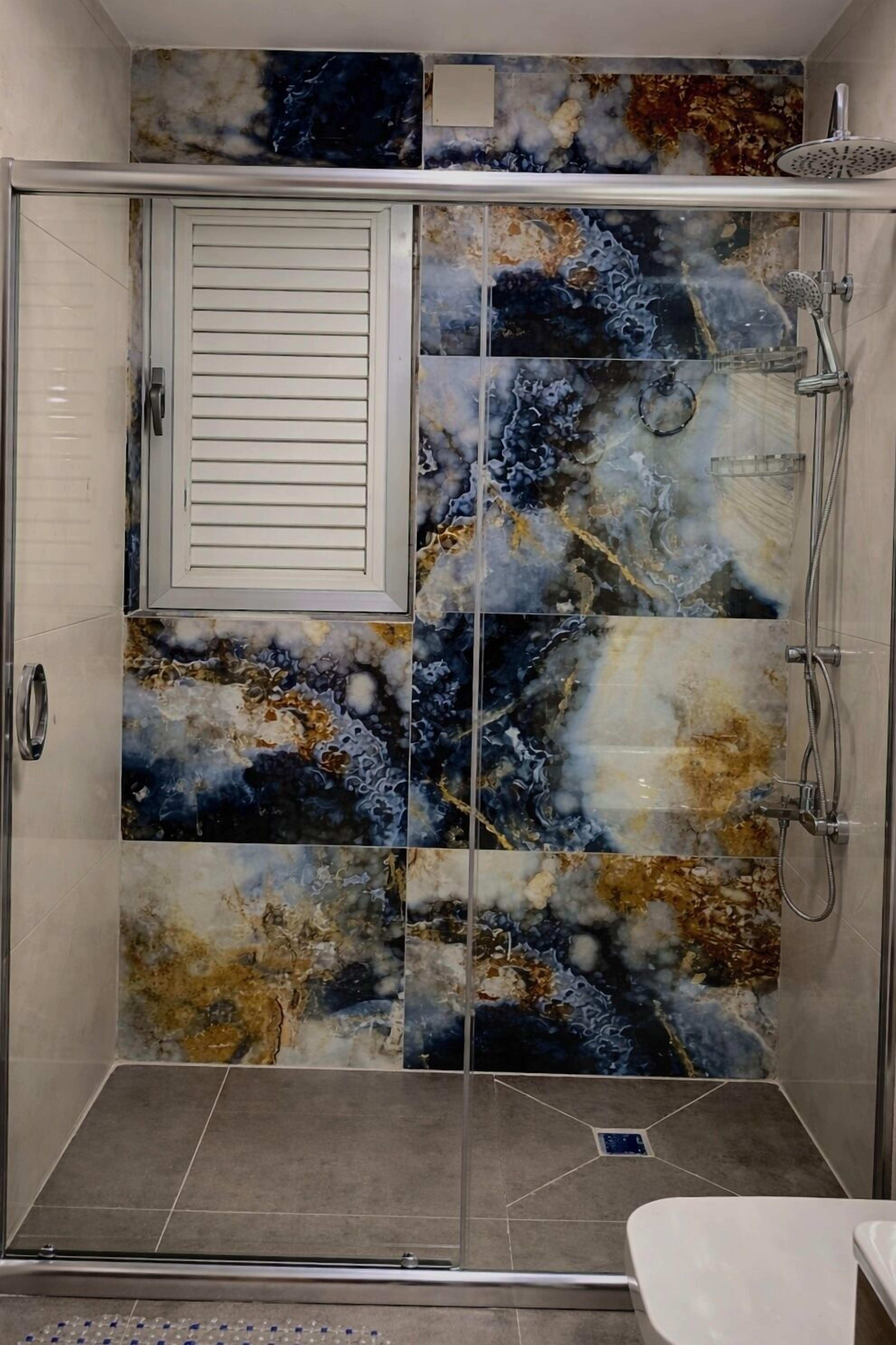 Een douche met een glazen deur en een wandontwerp van marmer.
