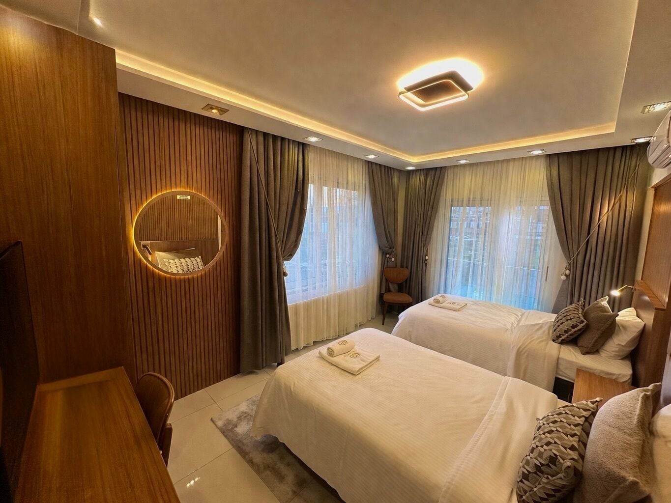 Una habitación de hotel con dos camas, un espejo redondo, un panel de madera en la pared y una lámpara en el techo.