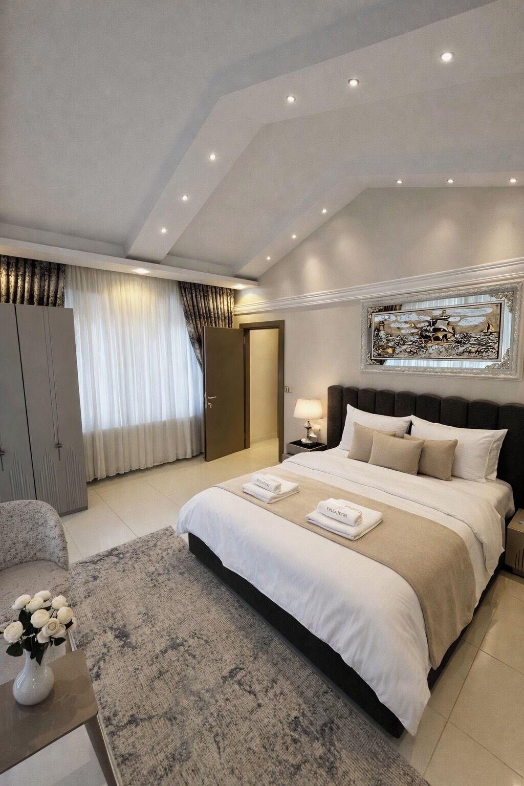 Un dormitorio de hotel moderno con una cama grande, un armario, una mesita de noche con lámpara y un cuadro decorativo en la pared.