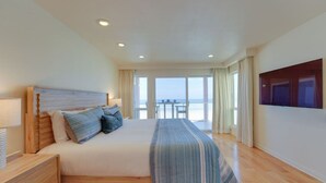A bedroom with a large bed, a nightstand, a TV, and a balcony with a view of the beach. - *New* Ocean Surf View | 2nd Floor Condo w/ Parking (San Diego)