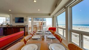 A dining area with a view of the beach, a kitchen with a TV, and a balcony with a pool. - *New* Ocean Surf View | 2nd Floor Condo w/ Parking (San Diego)