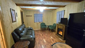 Ein gemütliches Wohnzimmer mit Holzboden, einem Ledersofa, einem kleinen runden Tisch, einem Holzesstisch mit Stühlen, einem Kamin und einem Fernseher.