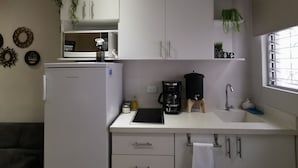 Eine kleine Küche mit weißen Schränken, einem Kühlschrank, einer Kaffeemaschine und einem Fenster mit Blick.