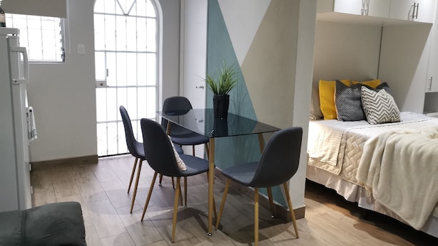 Ein modernes Zimmer mit einem Glastisch, zwei Stühlen, einem Bett mit gesteppter Bettdecke und einer Topfpflanze.
