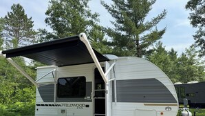 A white RV with a black awning, a sliding door, and a window. - New Northwoods Escape!  2026 Wildwood FSX Camper Near Bike Trails, Lakes & Pines (Boulder Junction)
