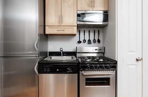 A compact kitchen with stainless steel appliances, including a refrigerator, microwave, stove, and sink.