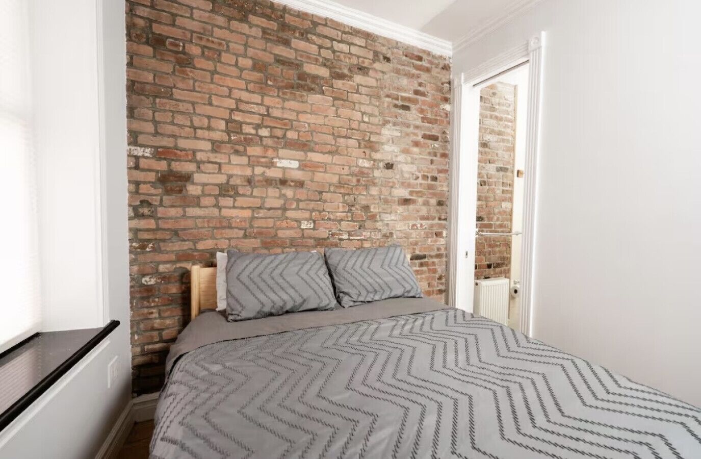 Ein Schlafzimmer mit Backsteinwand, einem Bett mit gemusterten Textilien und einer weißen Tür.