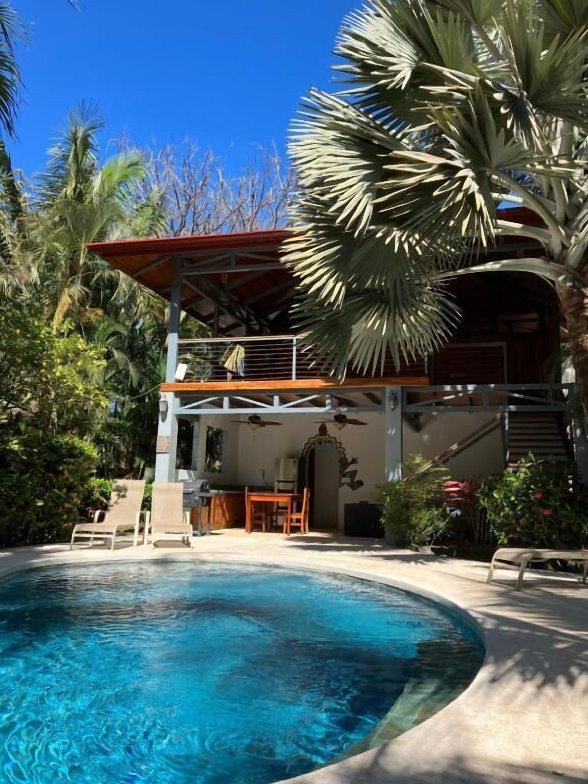 A poolside area with a covered seating area, a dining table, and a staircase leading to an upper level.