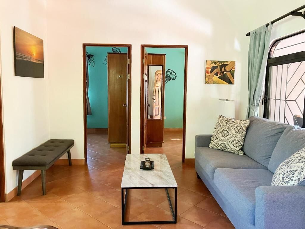 A living room with a sofa, a coffee table, a bench, and two doors leading to other rooms.