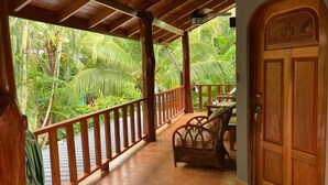 A wooden balcony with a railing, a wicker chair, and a door with a carved design. - Villa Tortuga Nosara (Playa Guiones)